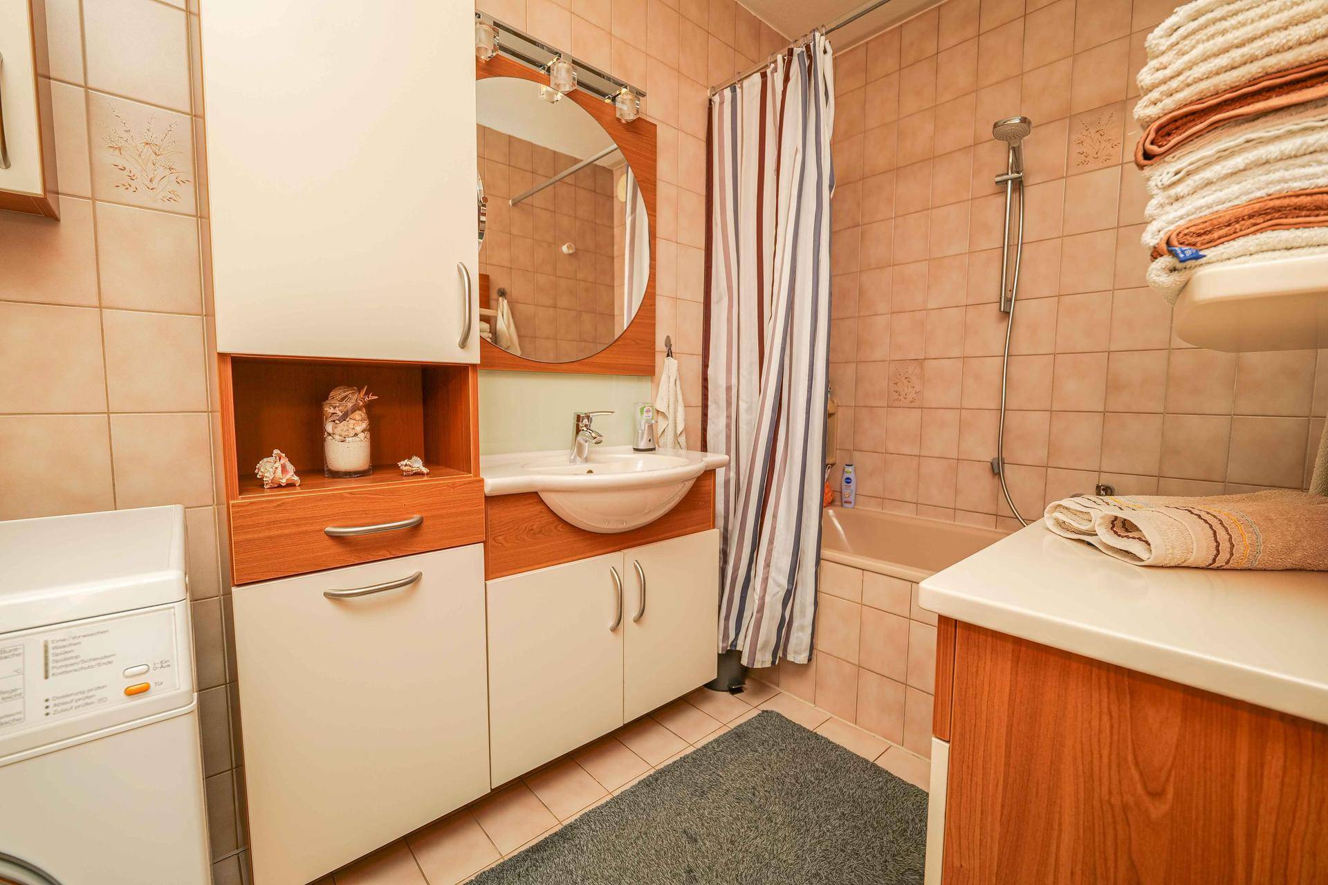Gefliestes Badezimmer mit Badewanne, Waschbecken und integrierter Waschmaschine.