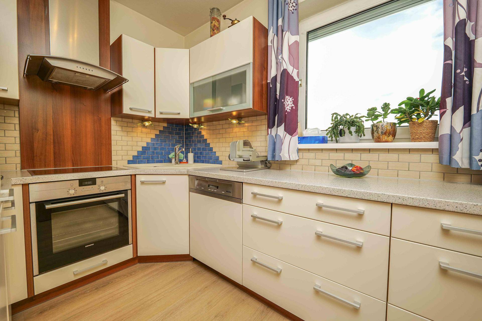 Kompakte Küche mit hellen Schränken, blauen Fliesen und integrierten Geräten.