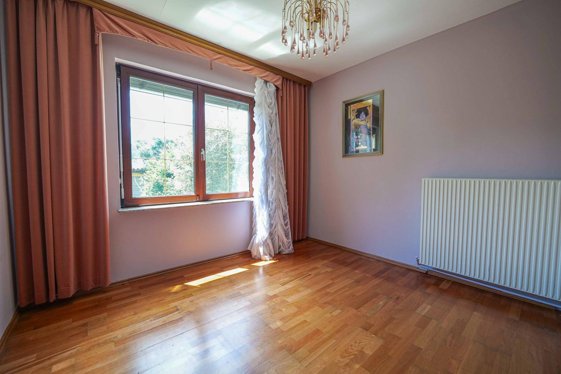 Helles Zimmer mit Holzboden, rosa Wänden und großem Fenster mit Vorhängen, ideal als Schlafzimmer.