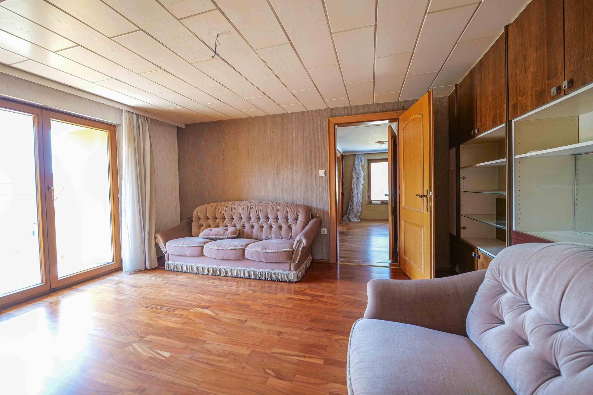 Geräumiges Wohnzimmer mit Holzboden, zwei Sofas und Zugang zu einem weiteren Raum.
