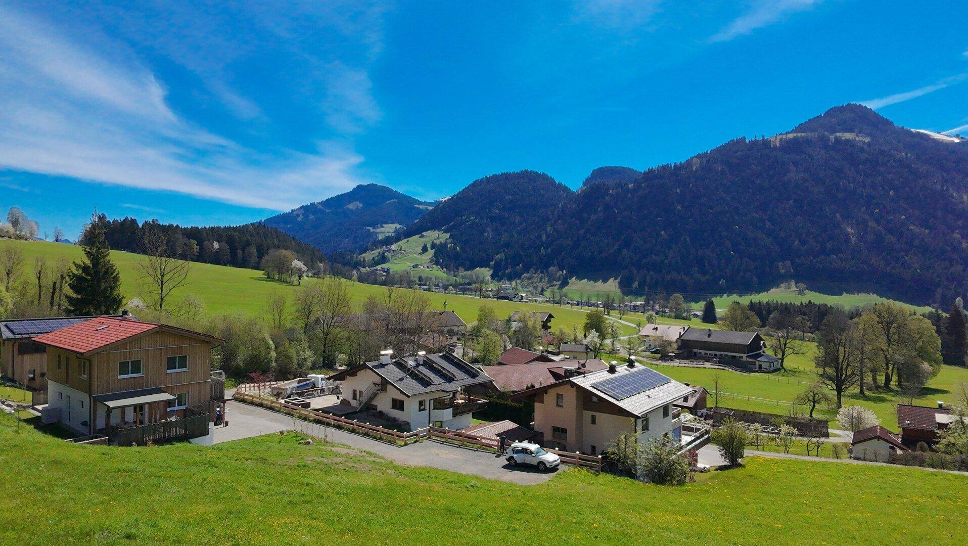 Idyllische Ansicht eines Bergdorfes mit traditionellen Häusern, grünen Wiesen und klarem Himmel.