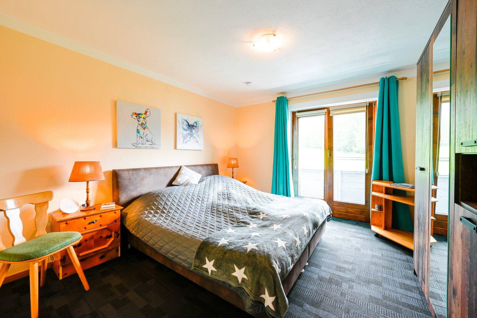Schlafzimmer mit großem Bett, dunklem Teppichboden und direktem Zugang zum Balkon.