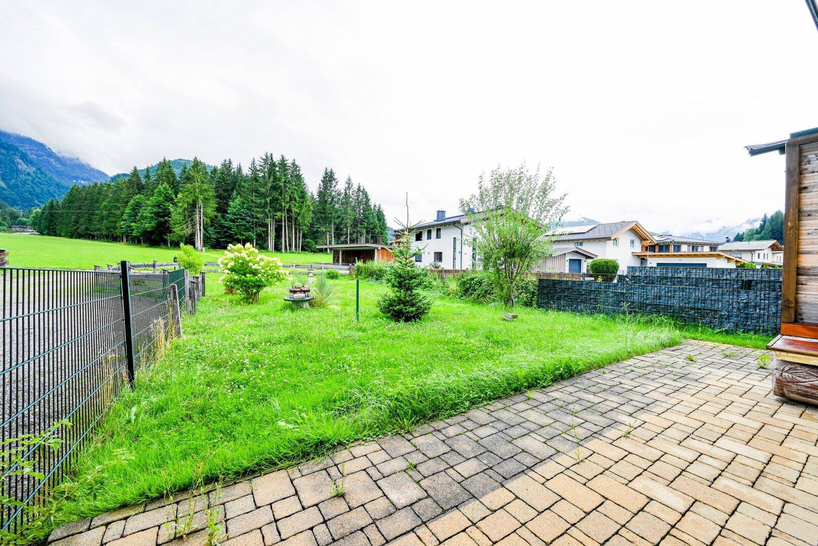 Gepflasterte Terrasse mit angrenzendem Rasenbereich und Blick auf die umliegende Natur.