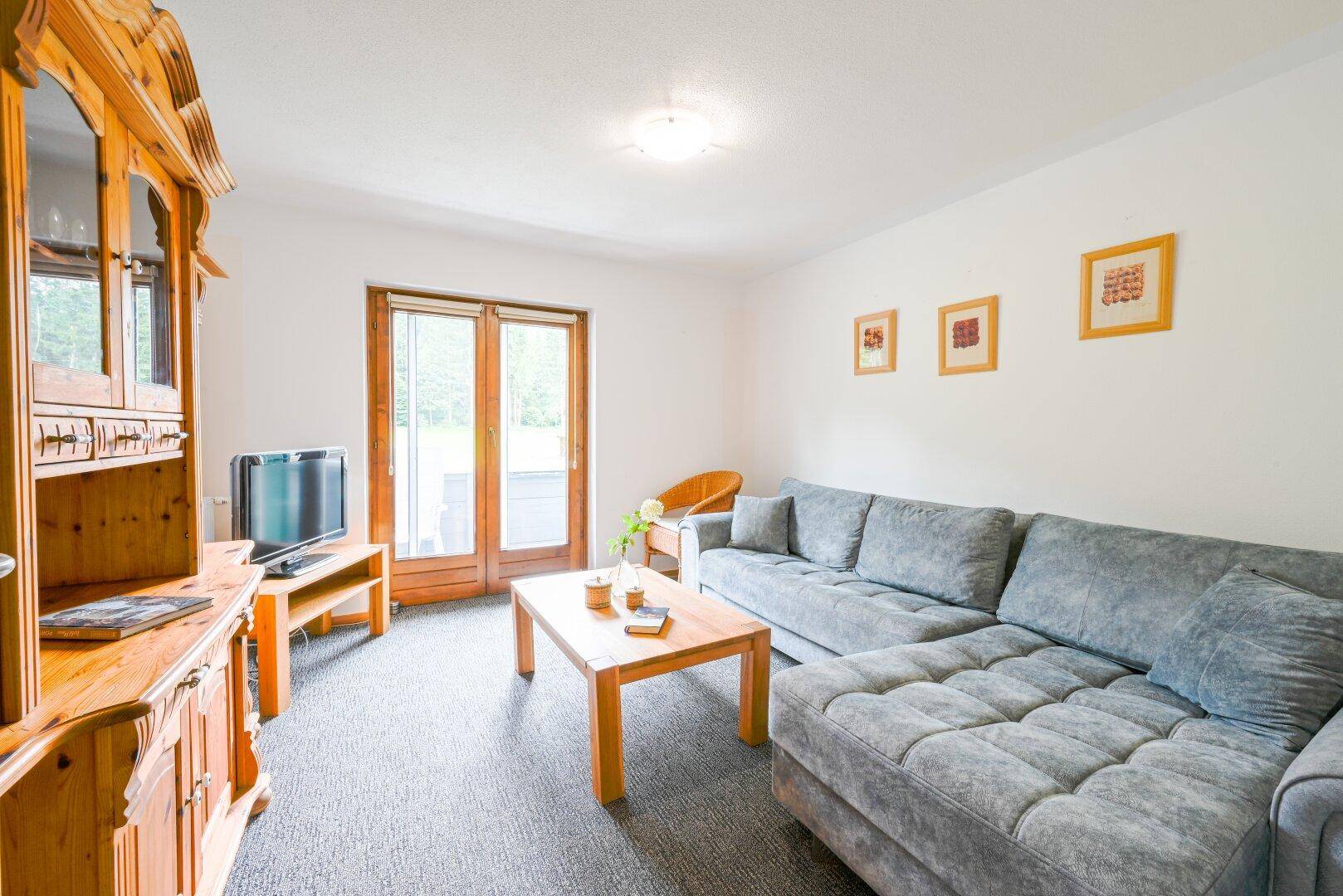 Wohnzimmer mit bequemer grauer Couch, Holzmöbeln und Zugang zu einem Außenbereich.