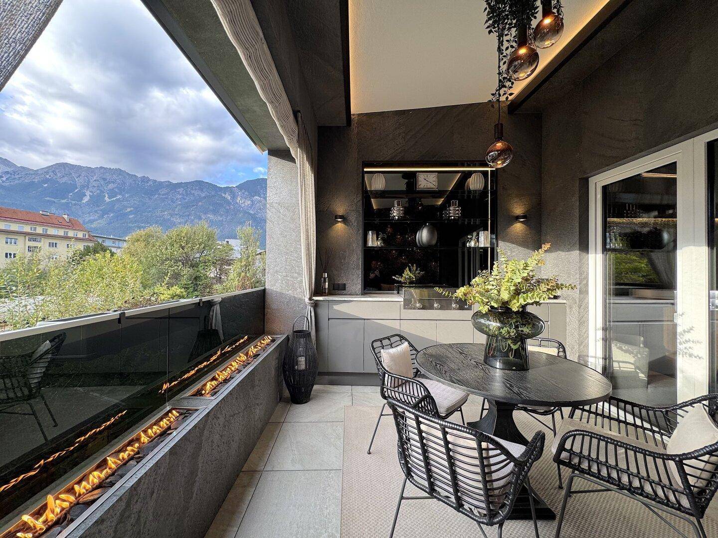 Großer Balkon mit Sitzgelegenheiten, Esstisch und Kamin mit Bergblick.