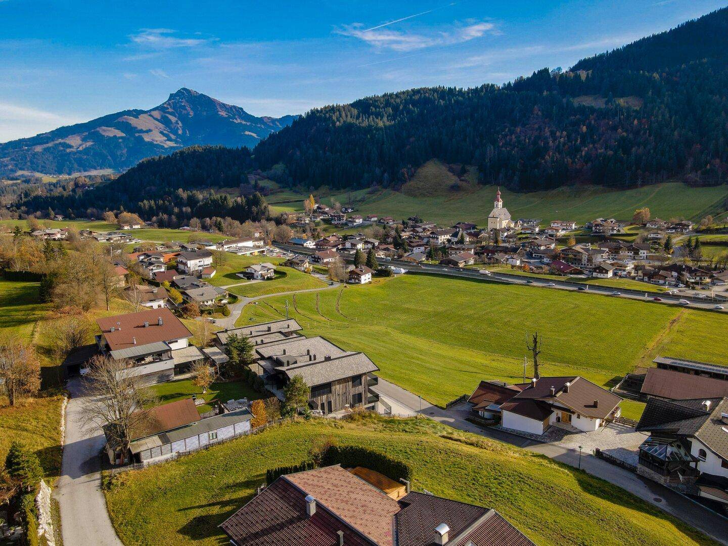 Luftaufnahme eines charmanten Dorfes mit Kirche, eingebettet in eine grüne Landschaft mit Bergen im Hintergrund.
