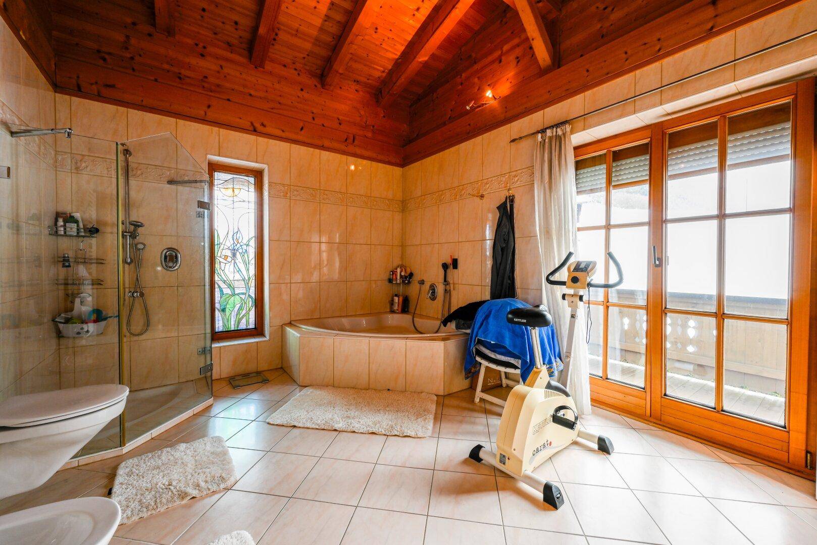 Großes Badezimmer mit Badewanne, Dusche, WC, Fliesenboden und Balkonzugang.