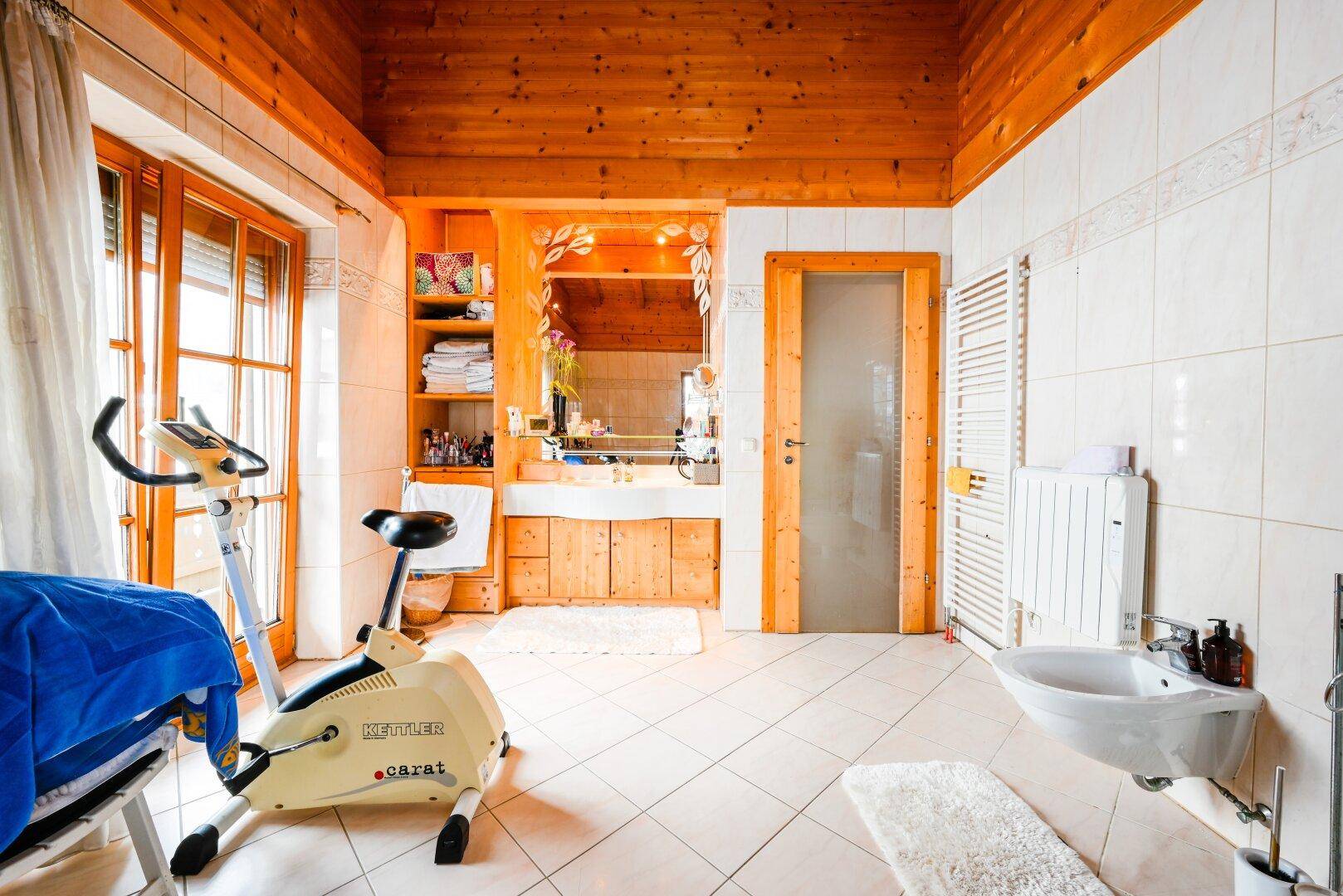 Geräumiges Badezimmer mit Holzbalkendecke, Fliesenboden, Einzelwaschbecken und Handtuchheizkörper.