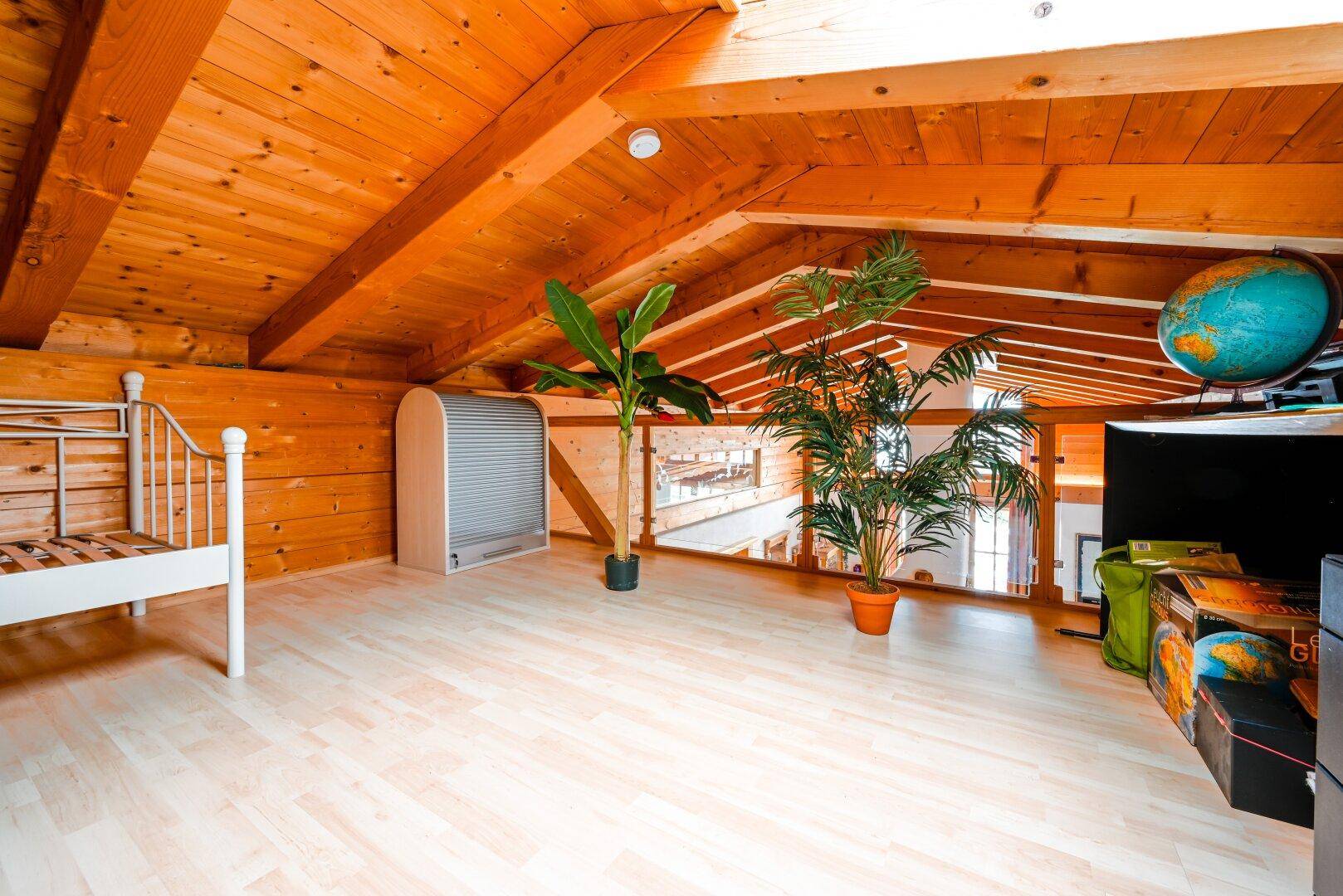 Offener Dachbodenbereich mit Holzbalken, hellem Laminatboden und Blick in den Wohnbereich.