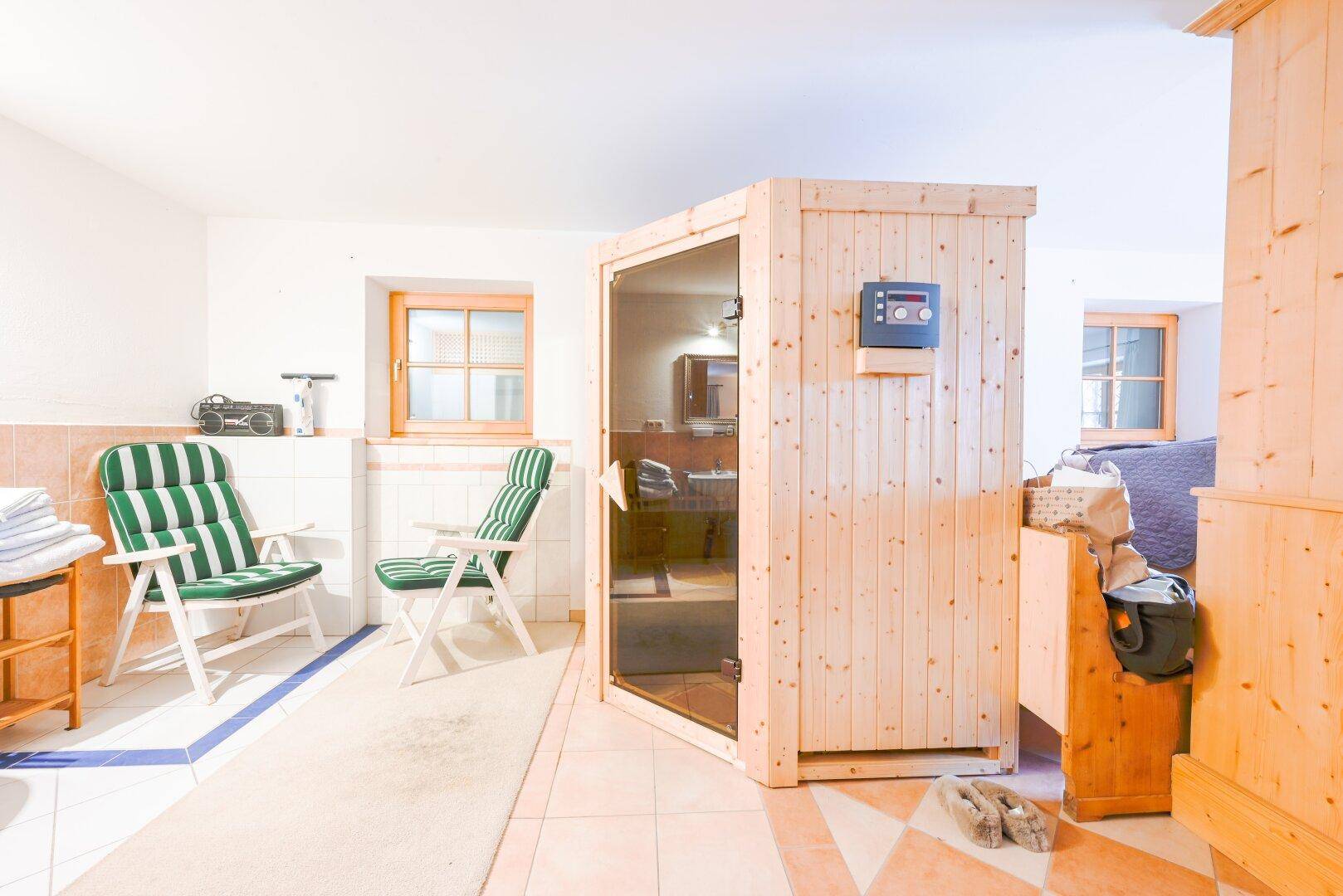 Entspannungsbereich mit Sauna, Liegestühlen, Fliesenboden und Fenster.