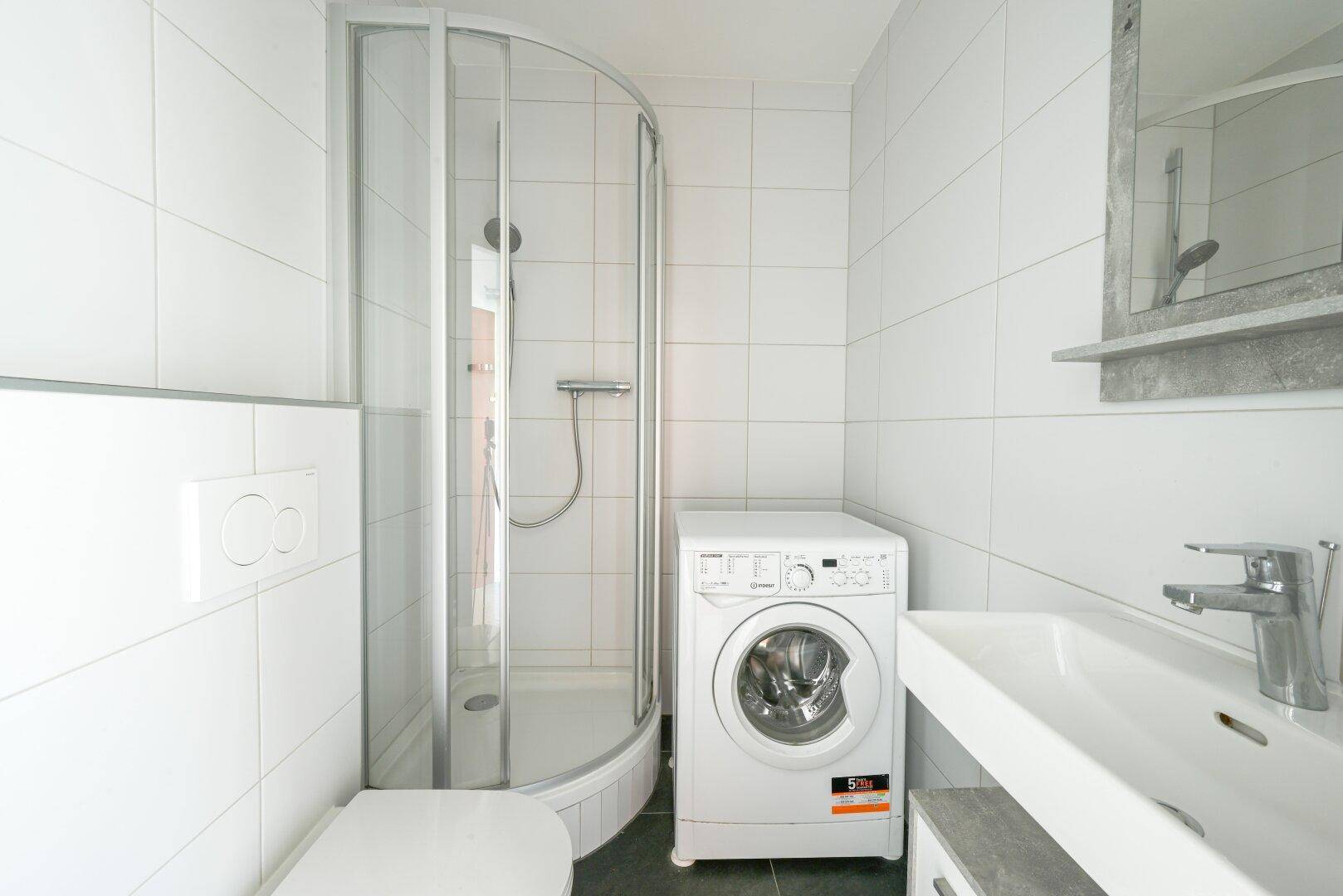Kompaktes Badezimmer mit Duschkabine, Waschbecken, Toilette und Waschmaschine.