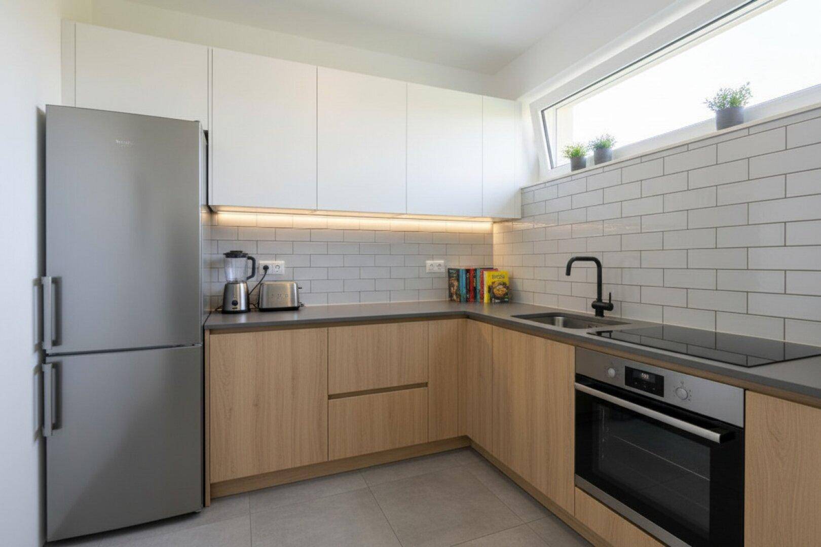 Moderne Küche mit hellen Holzfronten, weißen Oberschränken und integrierten Geräten.