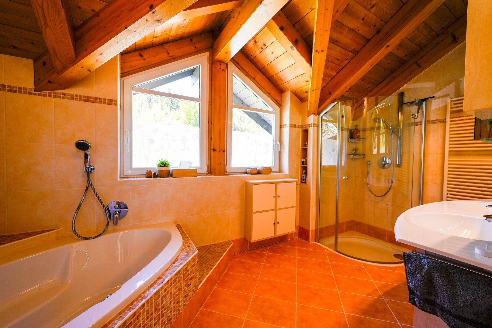 Geräumiges Badezimmer mit Badewanne, Dusche, Doppelwaschbecken und Holzbalkendecke.