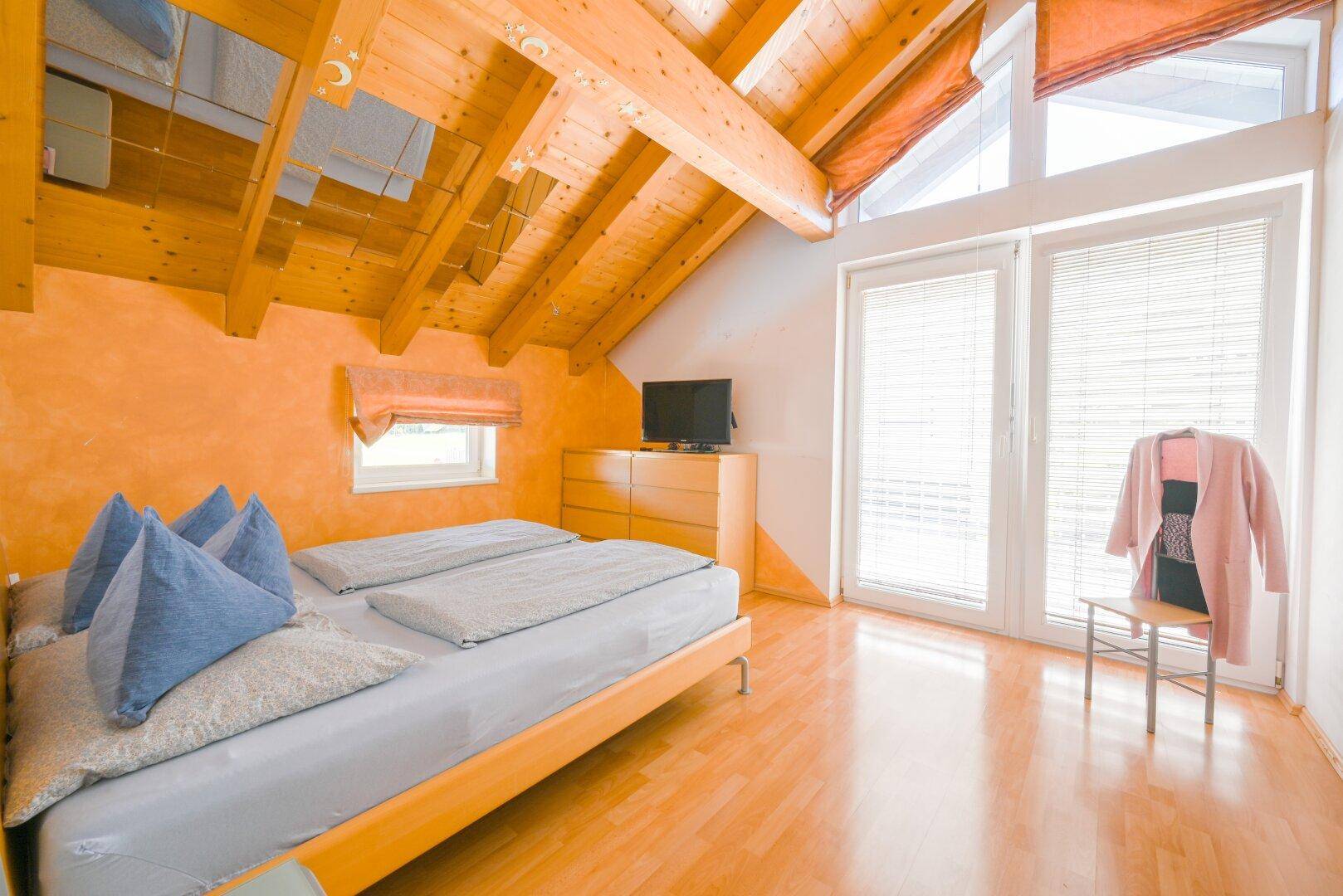 Gemütliches Schlafzimmer mit Holzbalkendecke, Parkettboden und Zugang zum Balkon.