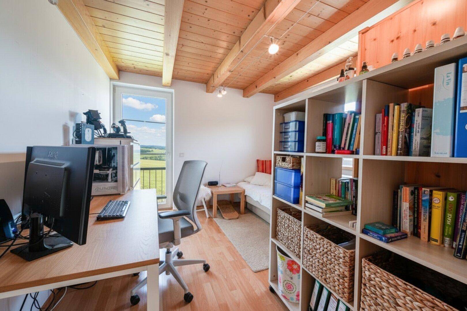 Arbeitszimmer mit Schreibtisch, Bücherregal, Holzbalkendecke und Blick ins Grüne.