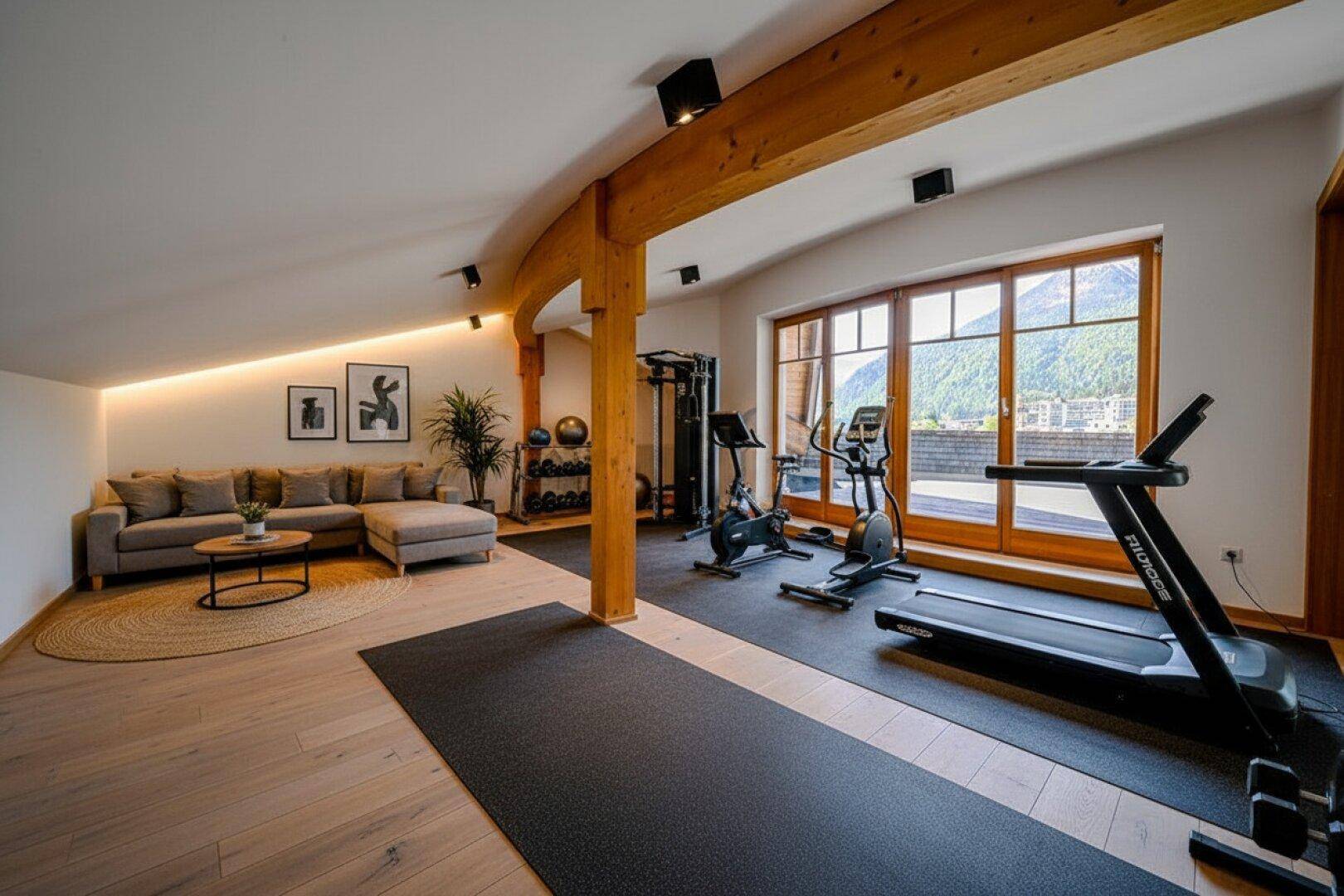 Fitnessraum mit Trainingsgeräten, Holzbalken und einem gemütlichen Loungebereich.