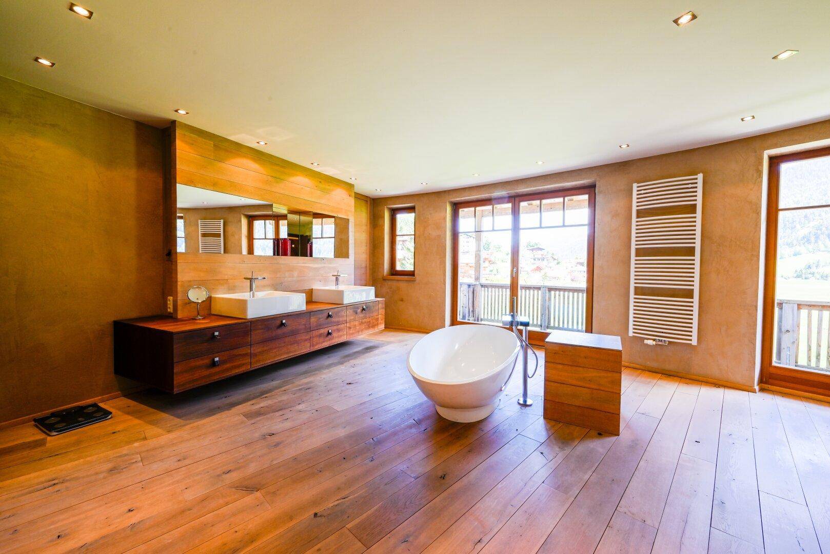 Luxuriöses Badezimmer mit freistehender Badewanne, Doppelwaschbecken und Holzboden.