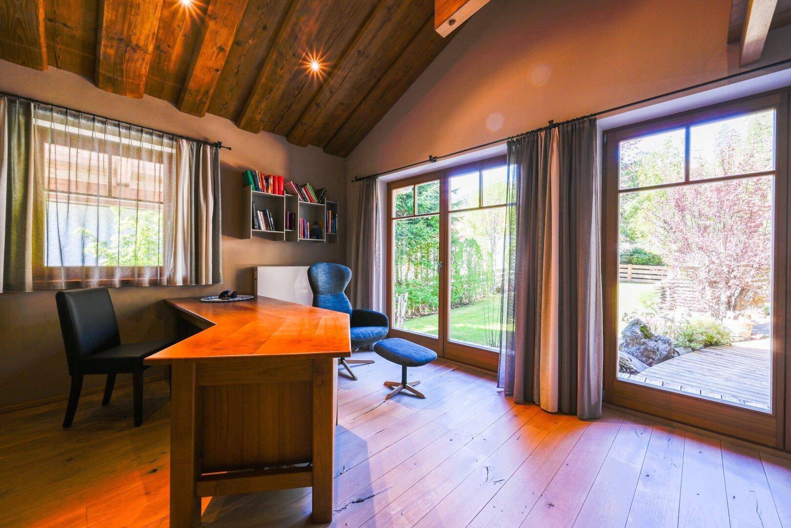 Arbeitszimmer mit Holzboden, Schreibtisch und großen Fenstern, die viel Tageslicht hereinlassen.