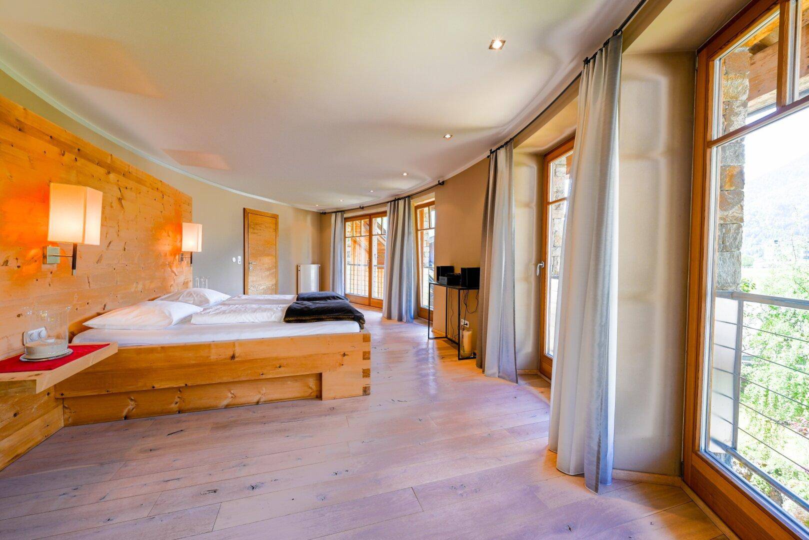 Helles Schlafzimmer mit Holzboden, Holzwänden und großen Fenstern mit Bergblick.
