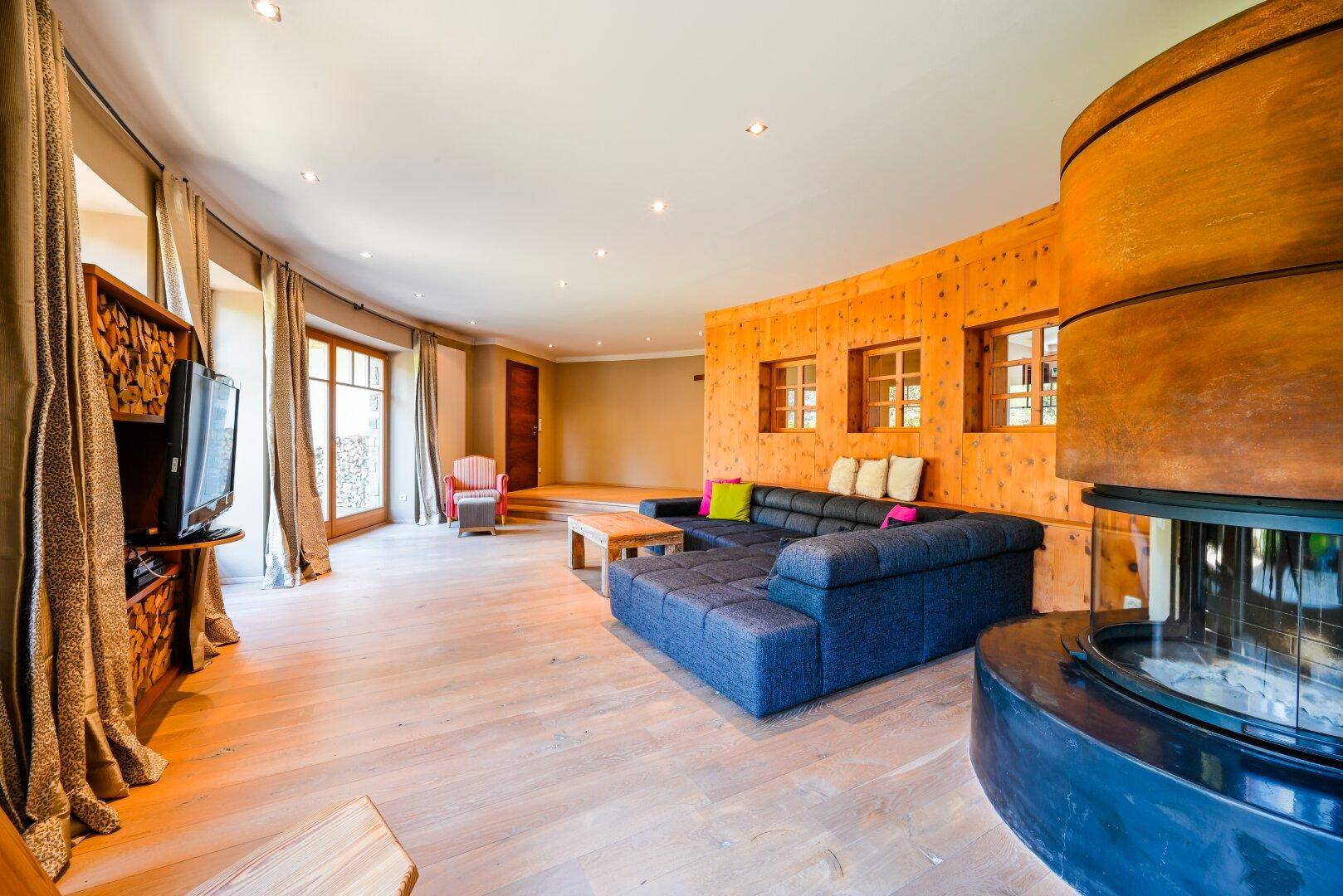 Geräumiges Wohnzimmer mit Holzwänden, modernem Sofa und einem runden Kamin in der Ecke.