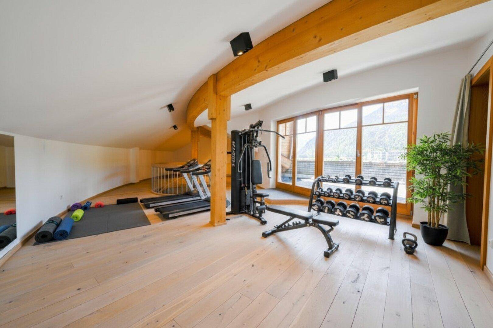 Geräumiger Fitnessraum mit verschiedenen Trainingsgeräten und Holzboden.