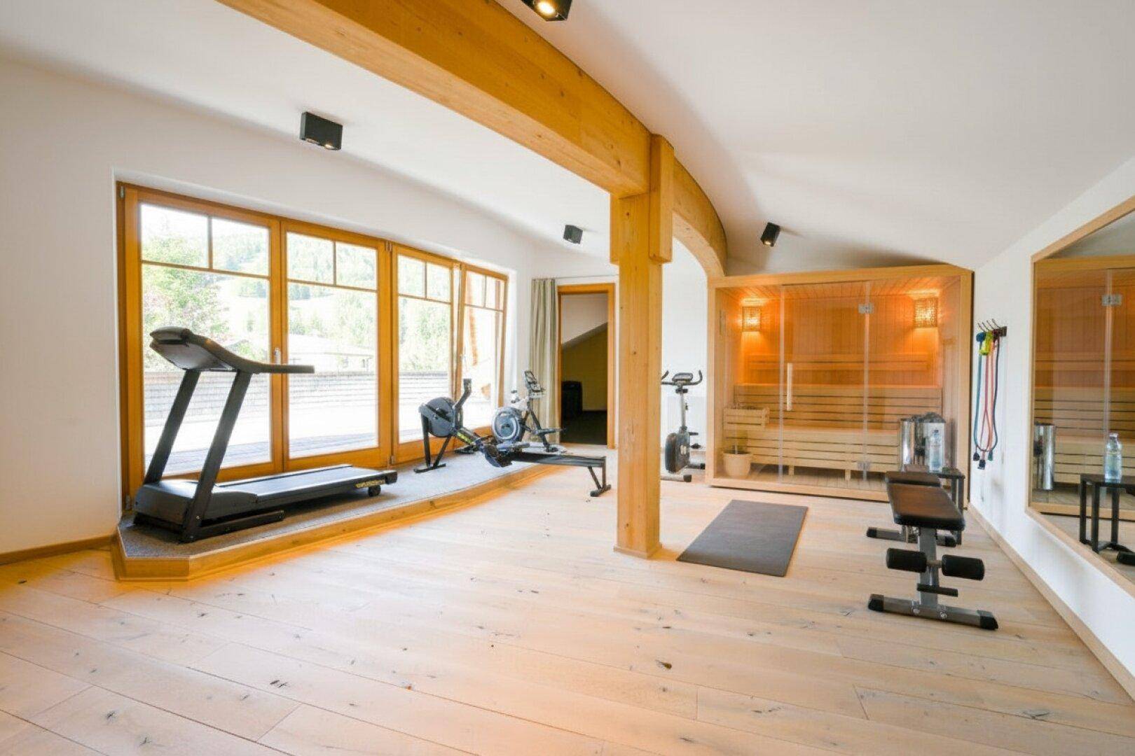 Fitnessraum mit Sauna, Trainingsgeräten und großen Fenstern mit Bergblick.