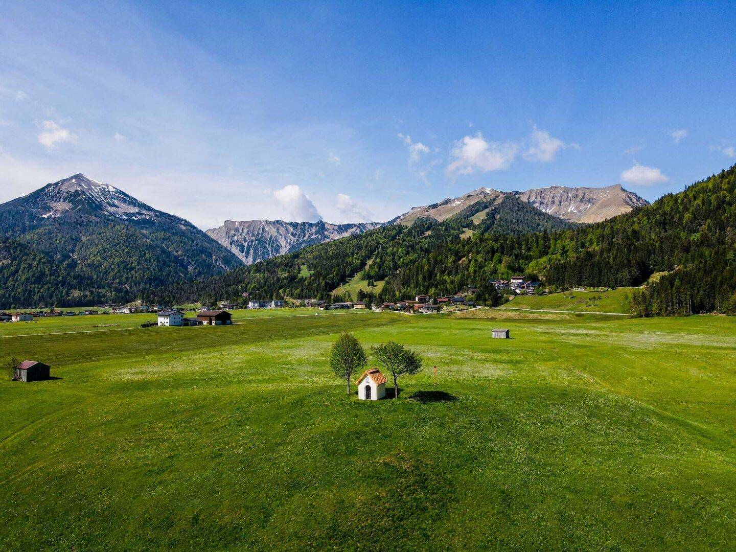 Luftaufnahme einer weiten grünen Landschaft mit Bergen und vereinzelten Häusern.
