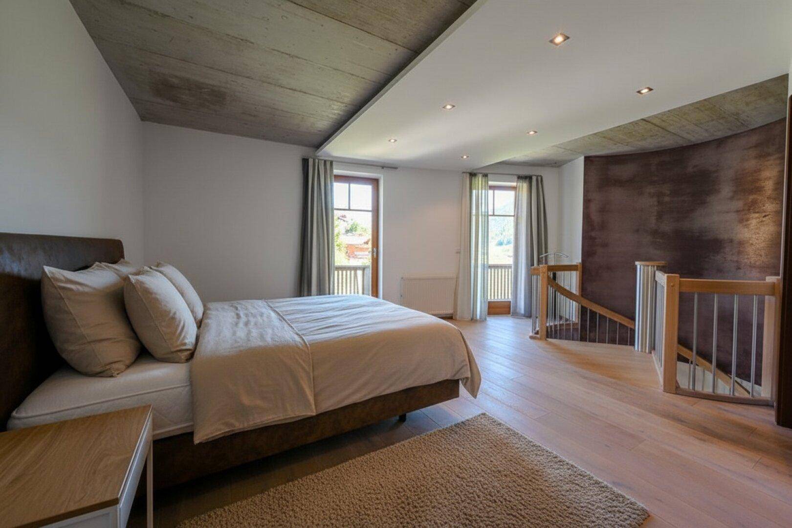Schlafzimmer mit Holzboden, Doppelbett und Zugang zu einem Balkon mit Bergblick.