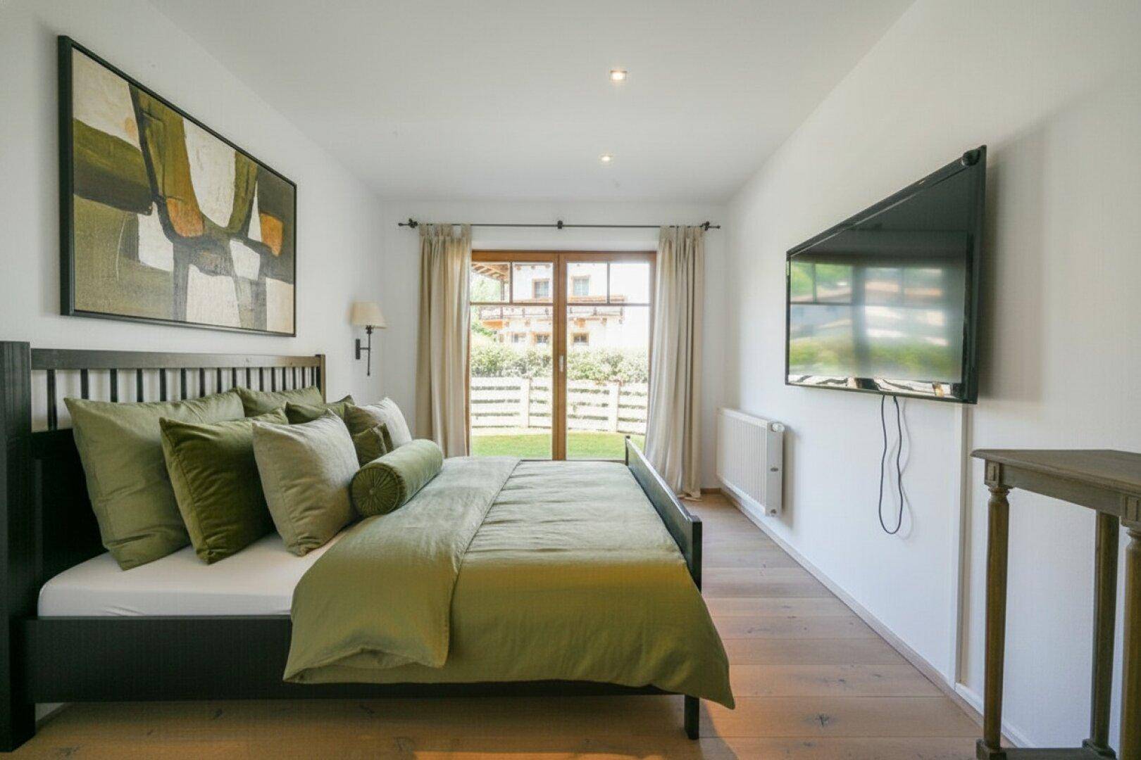 Modernes Schlafzimmer mit Holzboden, großem Bett und Zugang zu einem Balkon oder Garten.