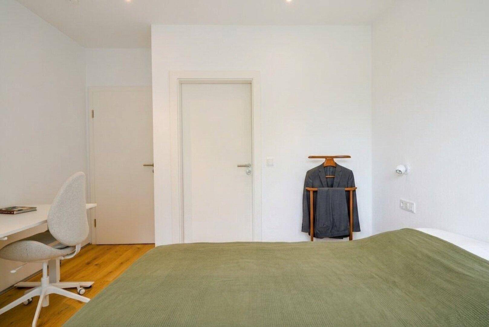 Helles Schlafzimmer mit Schreibtisch und Holzboden, ideal als Gäste- oder Arbeitszimmer.