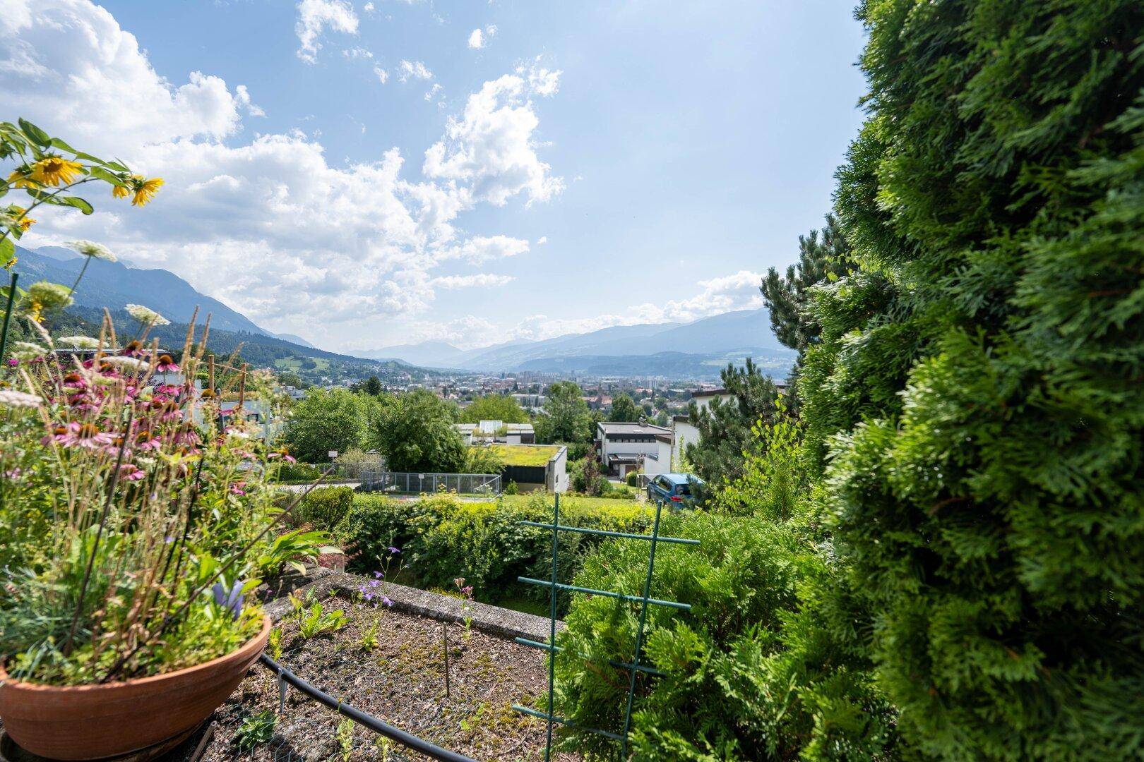 Panoramablick vom Garten über die Stadt und die umliegende Berglandschaft unter blauem Himmel.