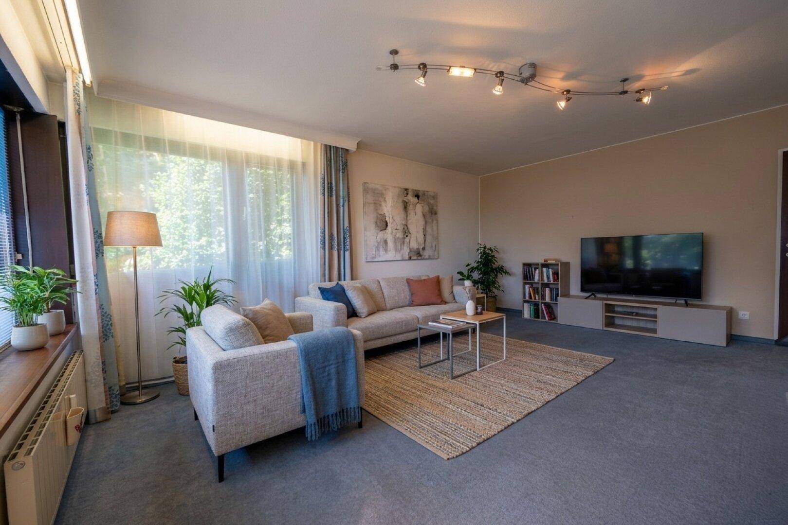 Gemütliches Wohnzimmer mit Teppichboden, bequemen Sofas und Pflanzen für eine wohnliche Atmosphäre.