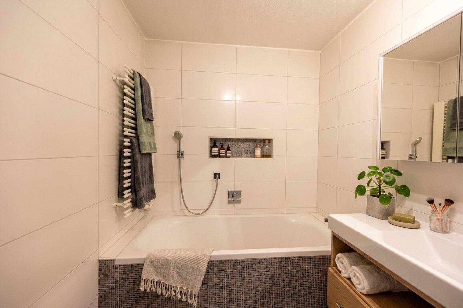 Modern gefliestes Badezimmer mit Badewanne, integrierter Nische und beheiztem Handtuchhalter.