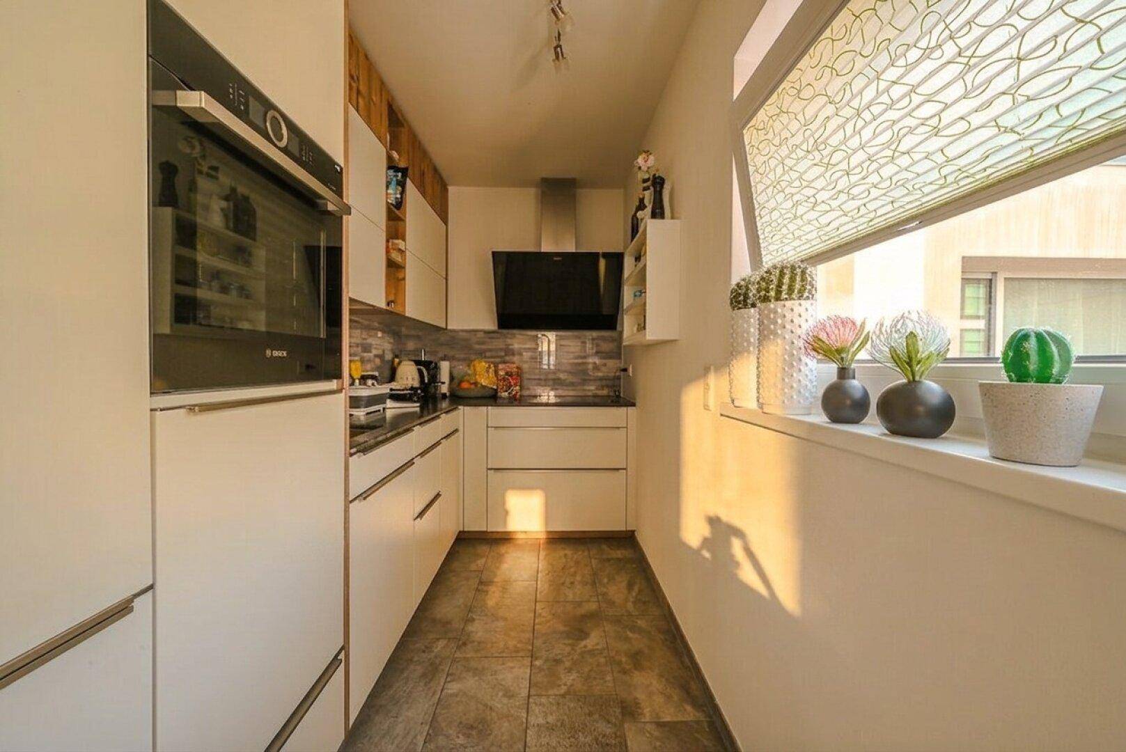 Moderne, schmale Küche mit Einbaugeräten, weißen Fronten und Fenster für Tageslicht.