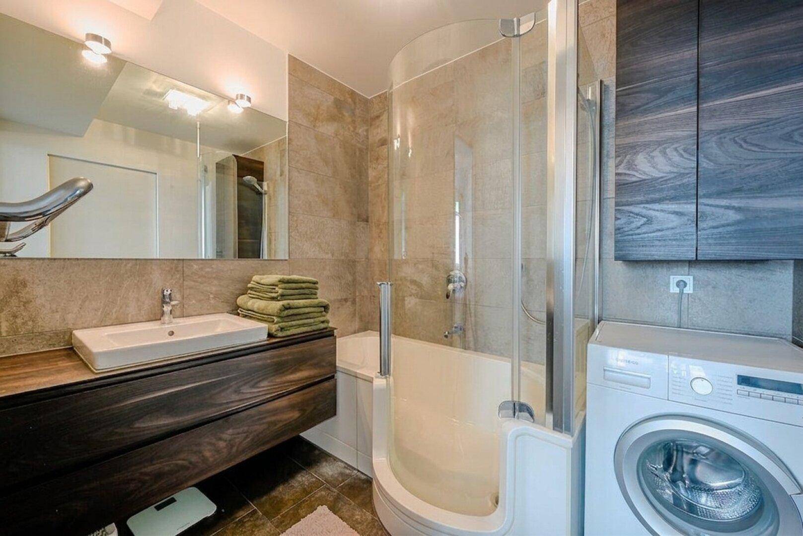 Modernes Badezimmer mit Dusche über der Badewanne, Einzelwaschbecken und Waschmaschine.
