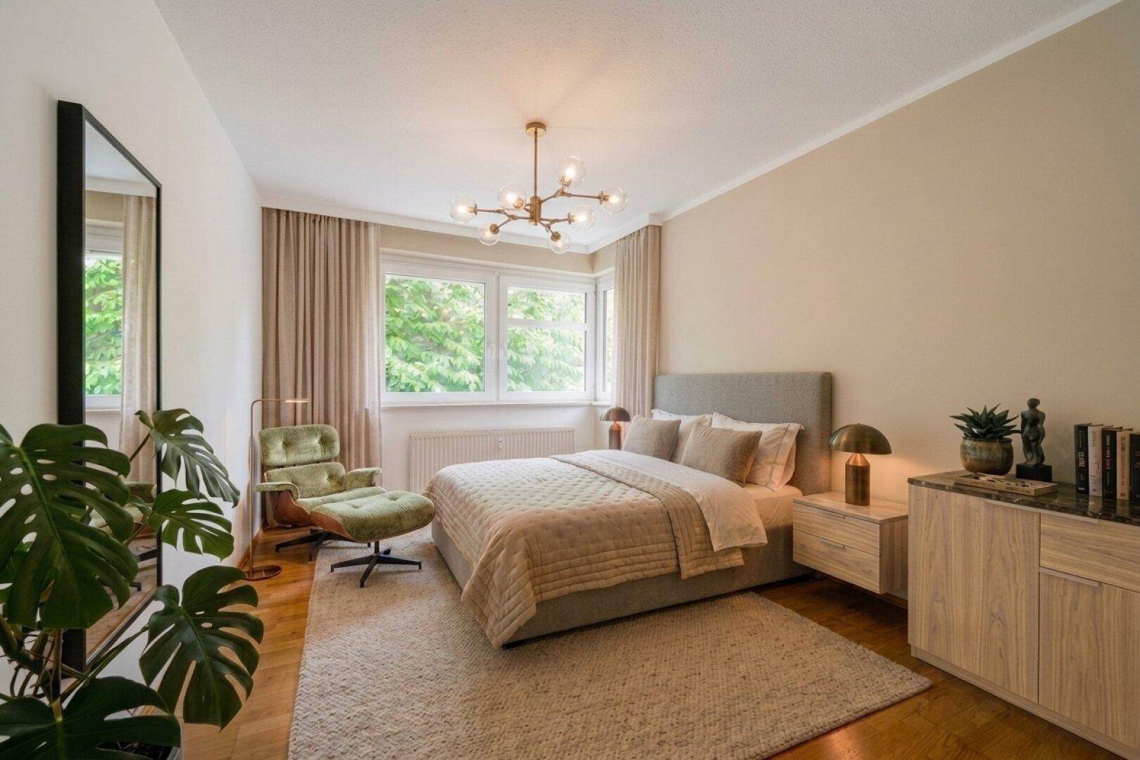 Ruhiges Schlafzimmer mit Doppelbett, Sessel und großen Fenstern mit Blick ins Grüne.