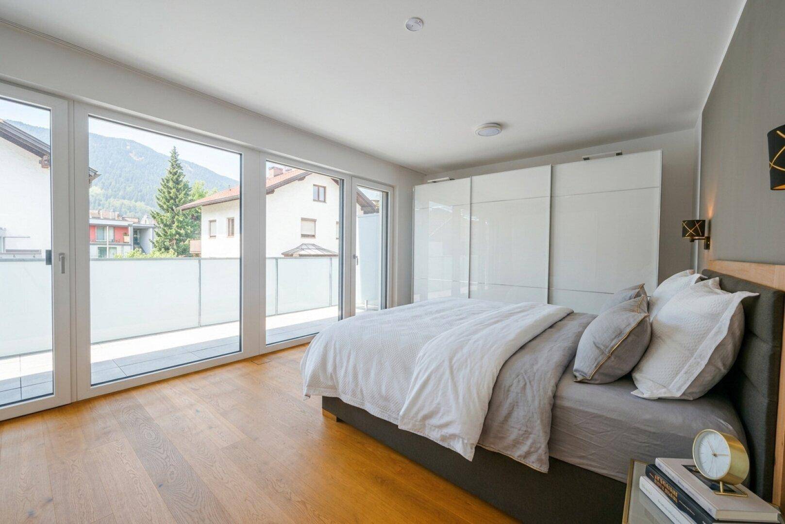 Helles Schlafzimmer mit Holzboden, großem Bett und Schiebetüren zum Balkon oder zur Terrasse.