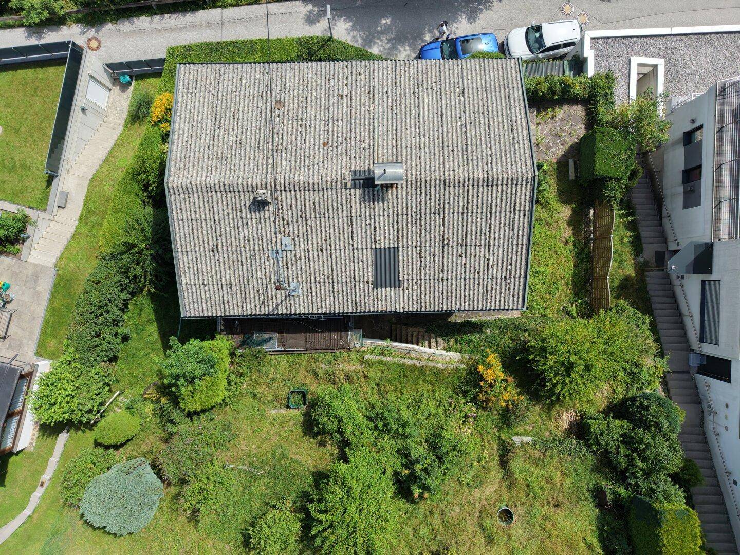 Senkrechte Luftaufnahme eines Hauses mit grauem Dach und umliegendem, dicht bewachsenem Gartenbereich.