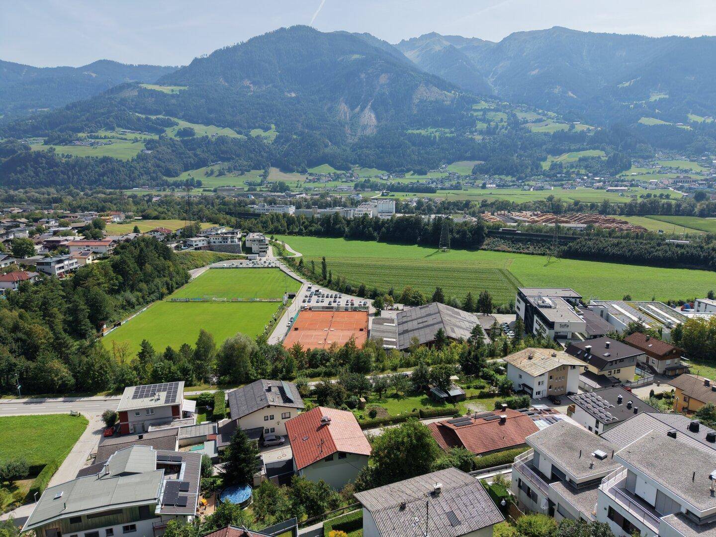 Panoramablick auf eine Wohngegend mit weiten Feldern und einer beeindruckenden Bergkulisse im Hintergrund.