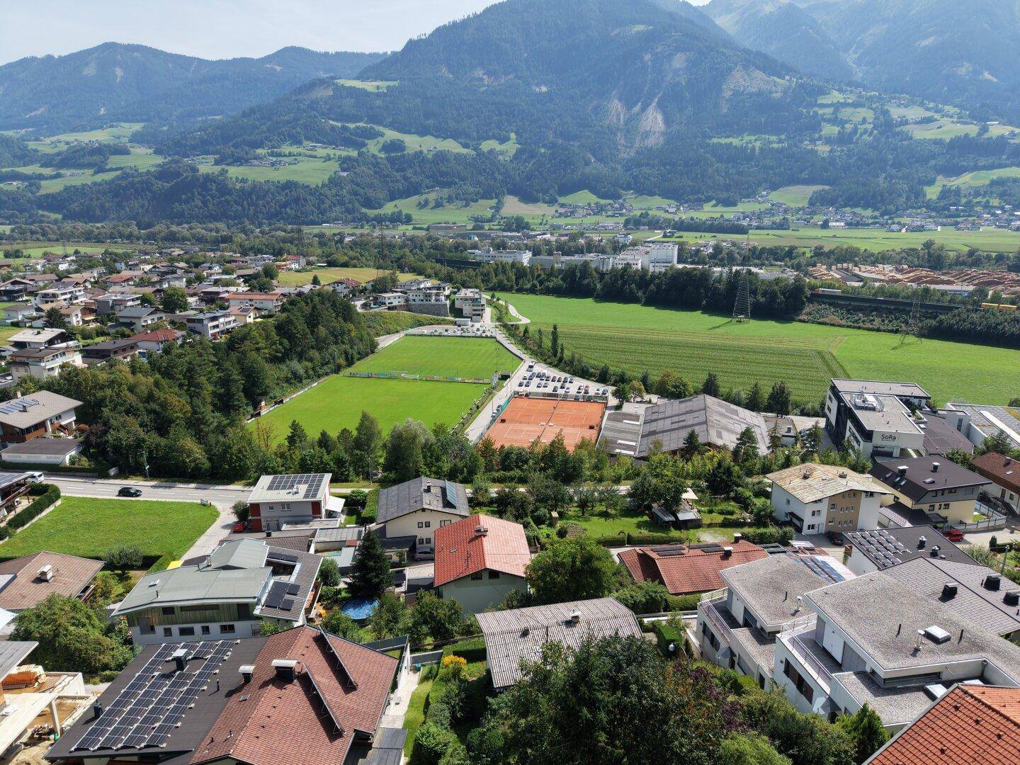 Ausgedehnte Ansicht einer Wohngegend mit Feldern, Sportplätzen und den majestätischen Alpen im Hintergrund.