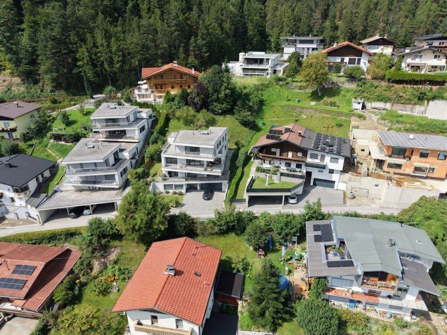 Überblick über eine Wohngegend mit verschiedenen Haustypen, eingebettet in eine grüne Hügellandschaft.