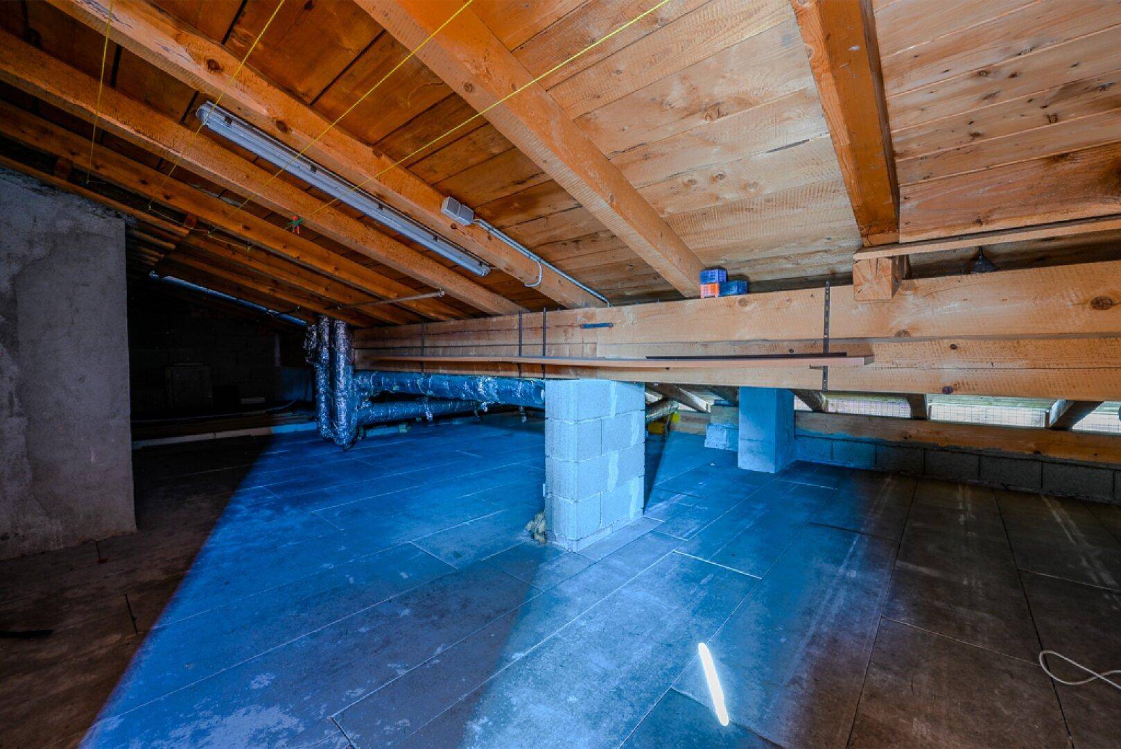 Unausgebauter Dachboden mit sichtbaren Holzbalken und Rohinstallationen.