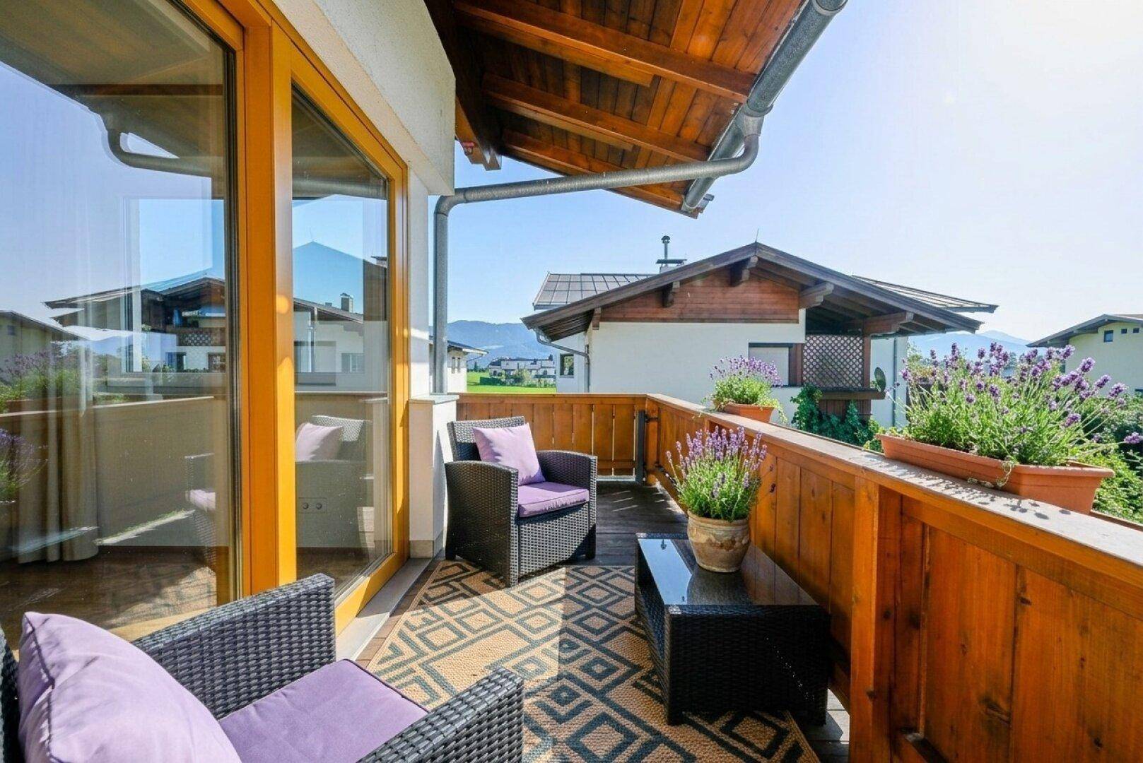 Sonniger Balkon mit Sitzgelegenheiten, Holzboden und Blick auf die Umgebung.