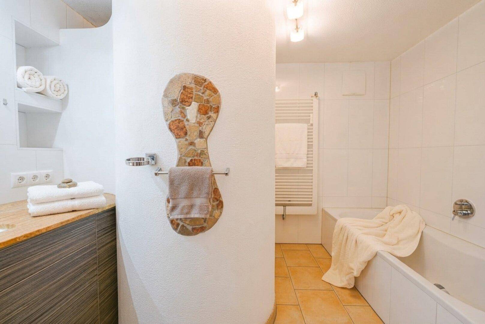 Badezimmer mit Badewanne, Waschtisch und beheiztem Handtuchhalter, hell gefliest.