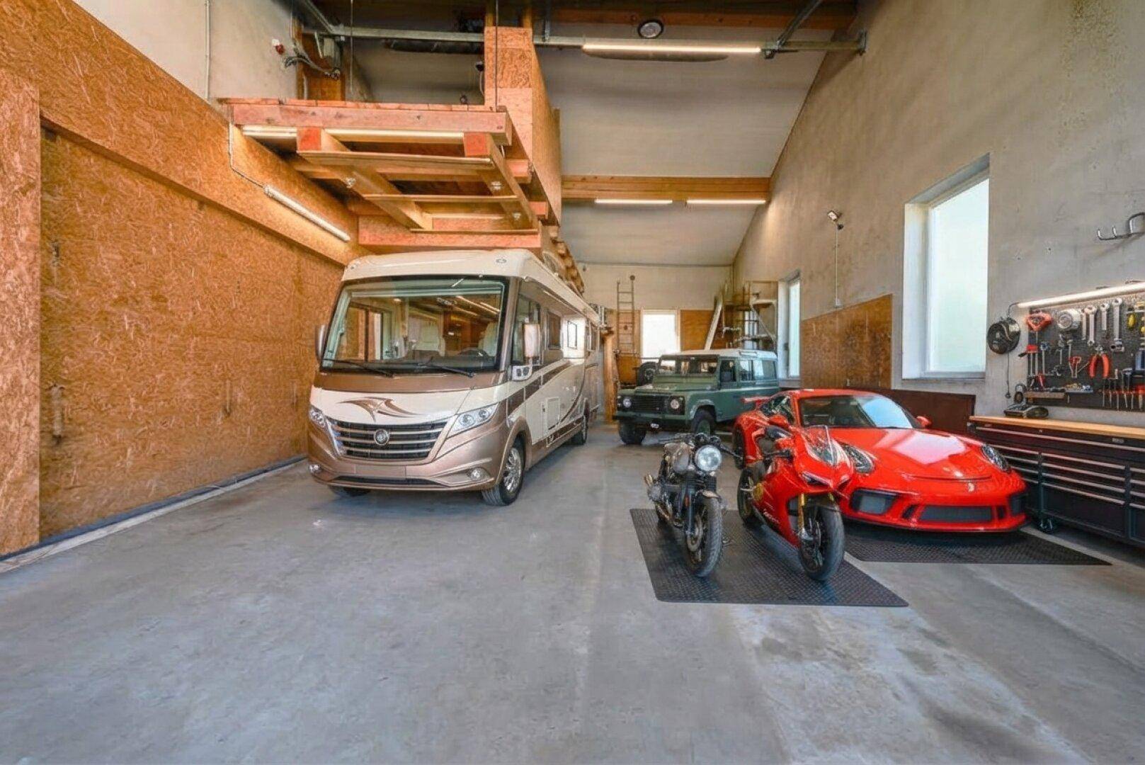 Große Garage mit modernem Wohnmobil, Geländewagen, Sportwagen und Motorrädern.