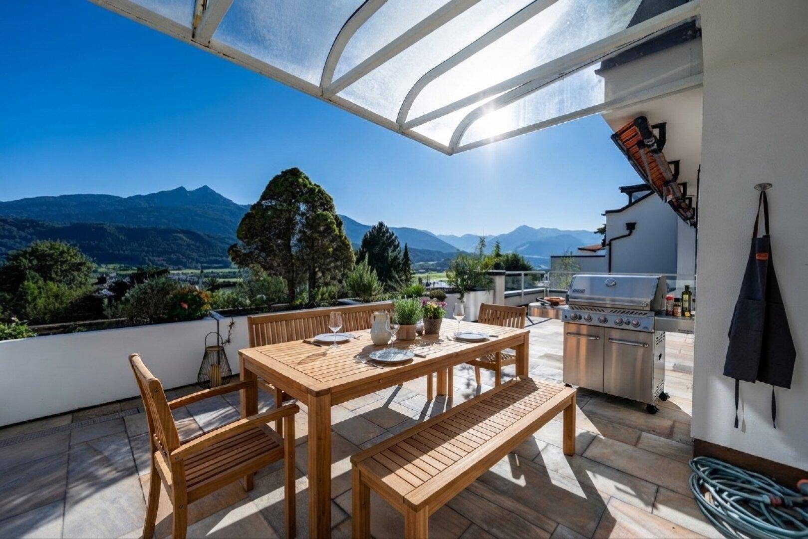 Geräumige Terrasse mit Esstisch, Grillbereich und Panoramablick auf die Berge.