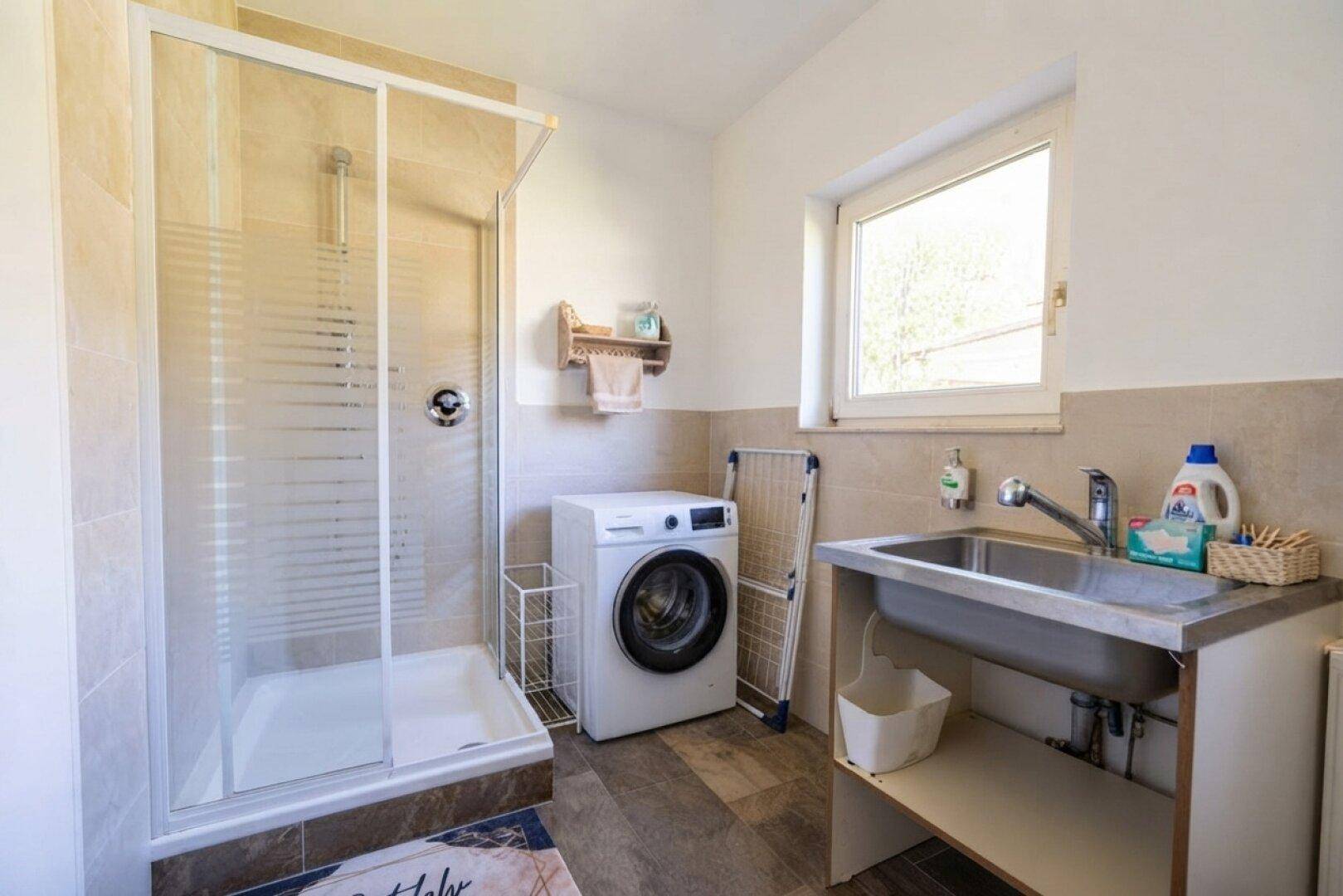 Praktischer Hauswirtschaftsraum mit Dusche, Waschmaschine und Spülbecken.