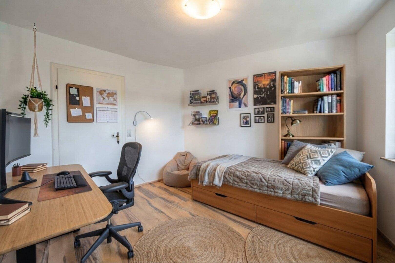 Jugendzimmer mit Holzboden, Schreibtisch und Bücherregal, ideal zum Schlafen und Lernen.