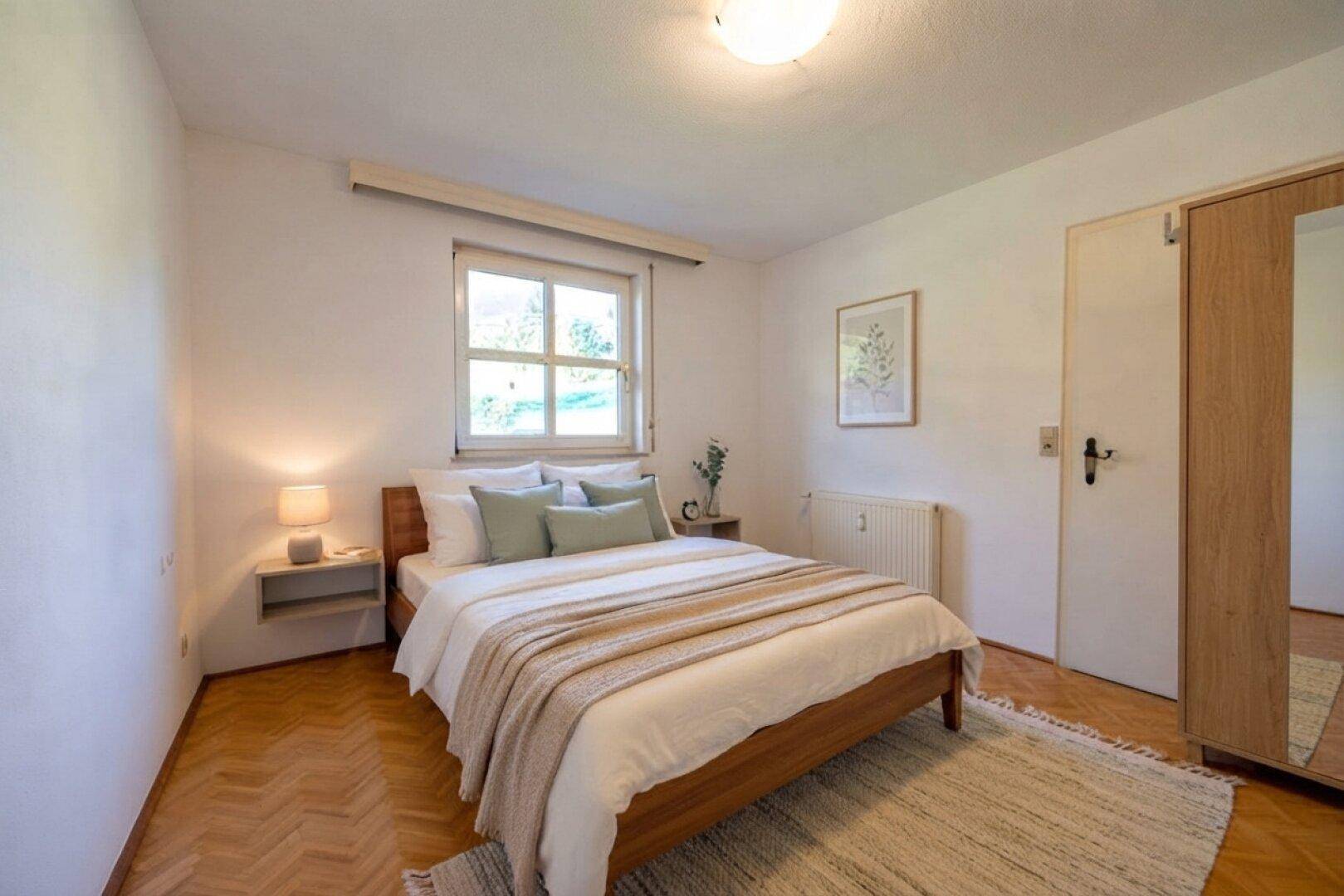 Gemütliches Schlafzimmer mit Holzboden, Doppelbett und Fenster mit Blick ins Grüne.