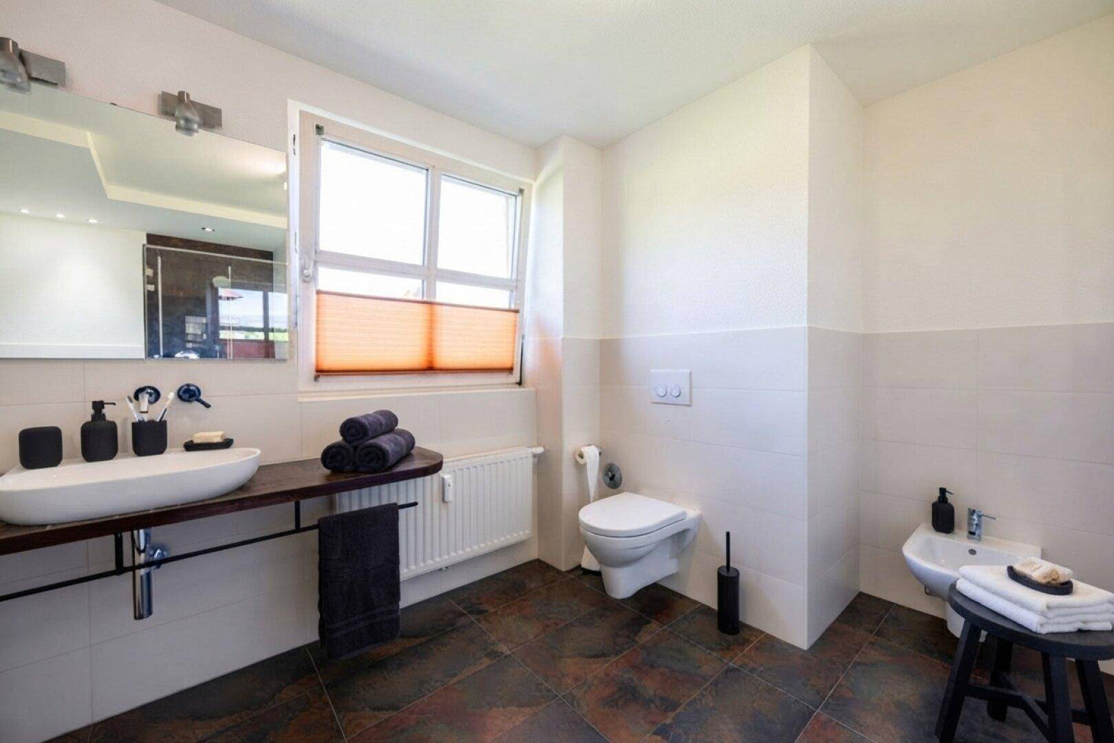 Helles Badezimmer mit modernem Waschbecken, Toilette, Bidet und Fenster.